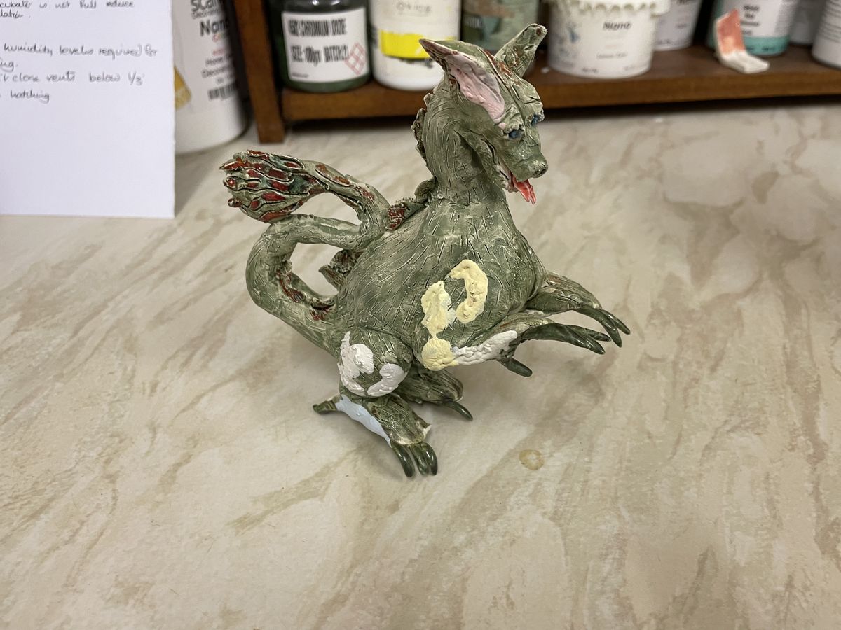 Small glazed ceramic dragon standing on a pale cloth
