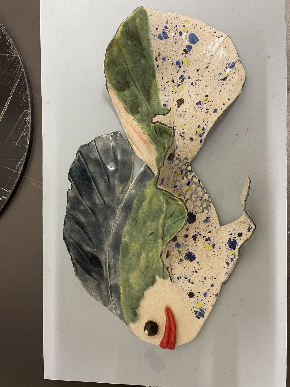 Ceramic relief of two overlapping leaves over a painted face