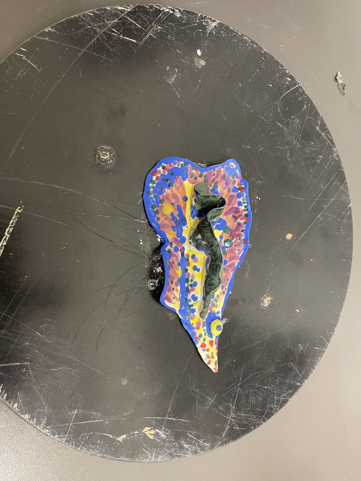 Heart-shaped ceramic mask painted in bright colours on a dark ground