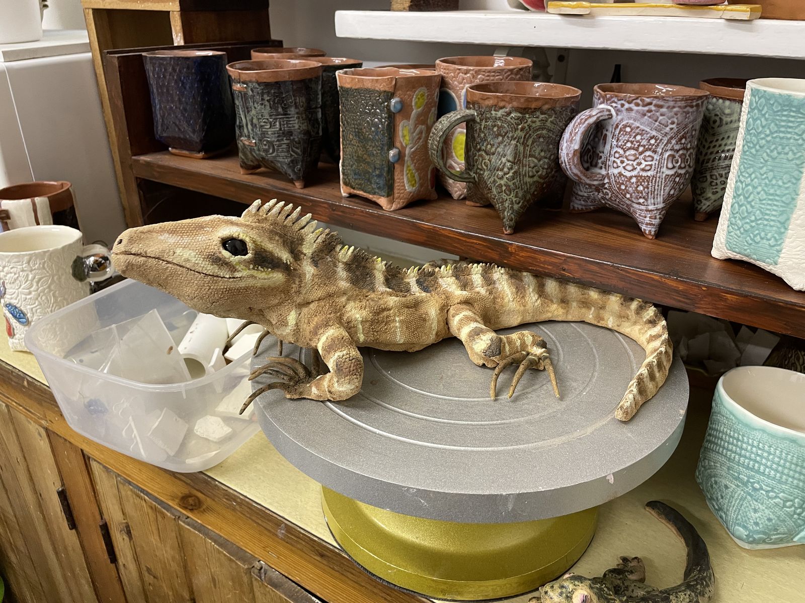 Studio bench with a carved crocodile sculpture surrounded by mugs and tools
